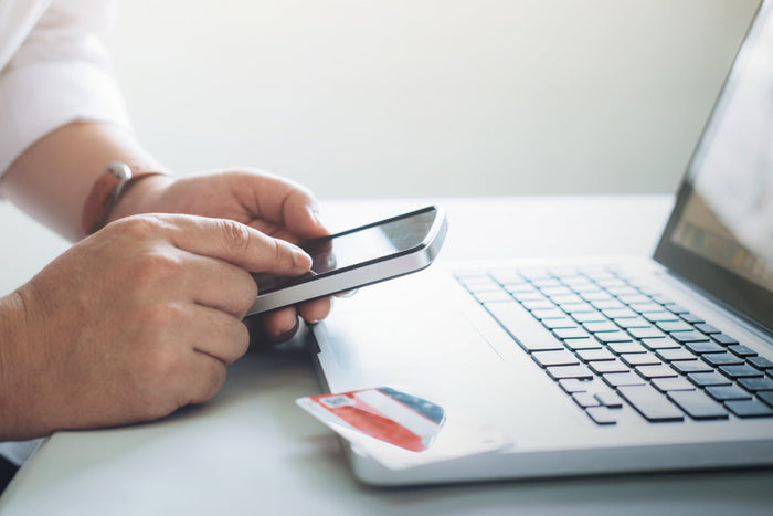 Person holding a smartphone with a credit card next to a laptop on a desk