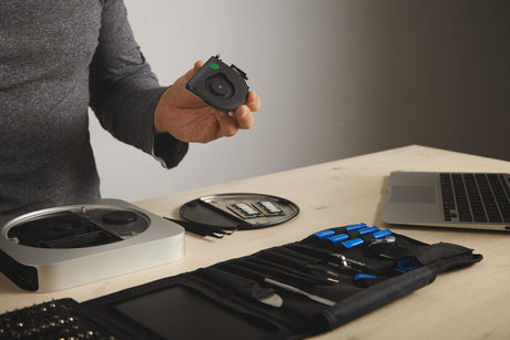 Person holding a small electronic device over a desk with computer components.