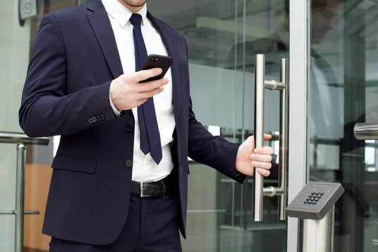 Man in a suit holding a phone, standing in front of a glass door.